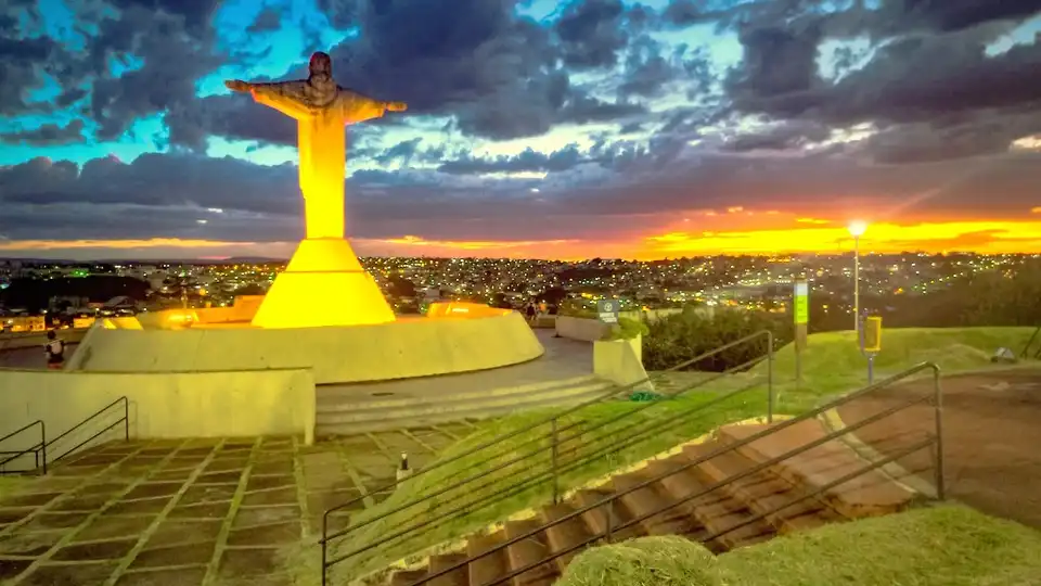 Cristo Redentor de Araxá, MG, iluminado ao entardecer no morro, com a cidade ao fundo