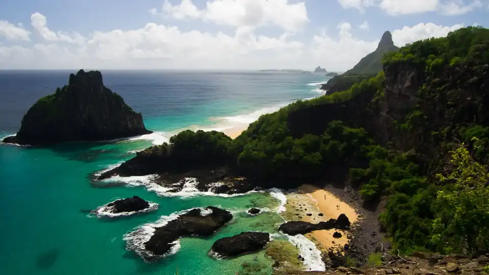 Vista panorâmica da Baía dos Porcos em Fernando de Noronha — águas esmeralda, rochas vulcânicas e Morro Dois Irmãos ao fundo