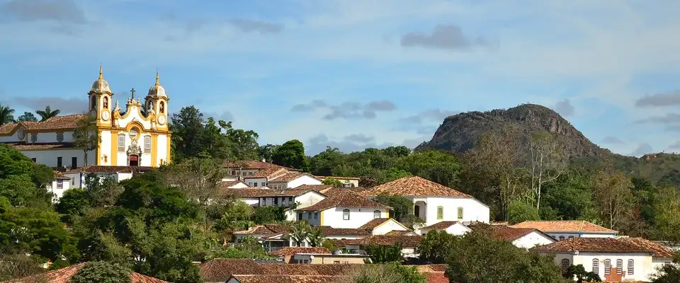 Tiradentes, MG — Igreja Matriz de Santo Antônio com fachada branca e amarela e casario colonial ao redor, com a Serra de São José ao fundo