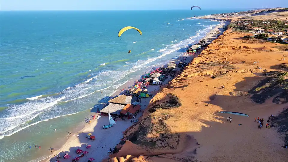 Vista aérea de Canoa Quebrada — falésias coloridas, praia e vila no litoral leste do Ceará
