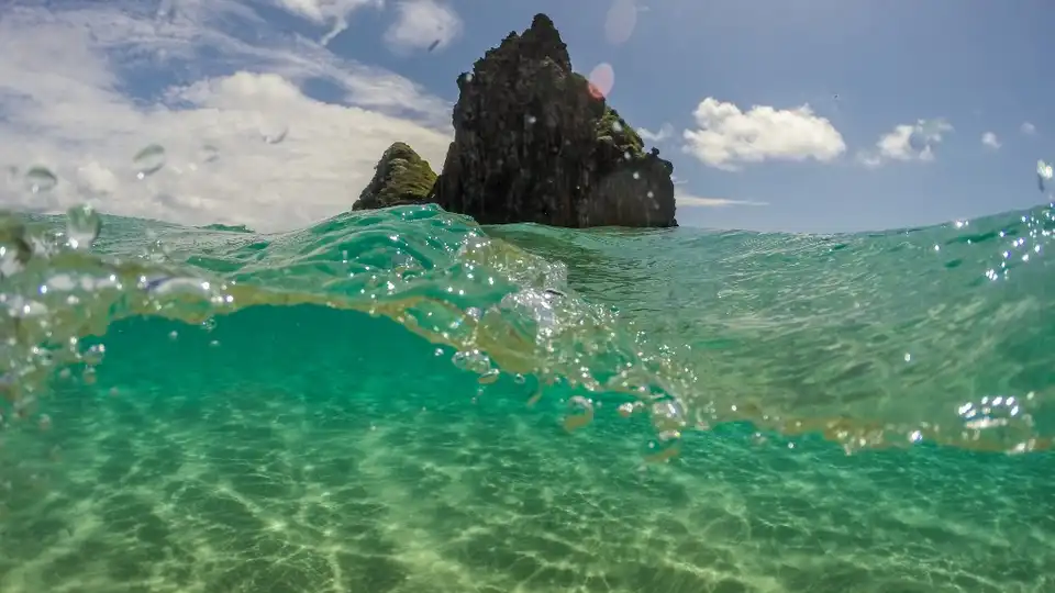 Praia do Sancho em Fernando de Noronha — foto meio a meio com águas cristalinas turquesa e formações rochosas ao fundo