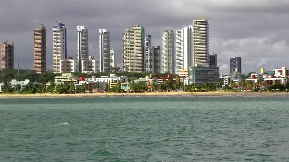 Praia de Cabo Branco em João Pessoa, PB — orla com prédios baixos na beira-mar, coqueiros e mar verde-esmeralda
