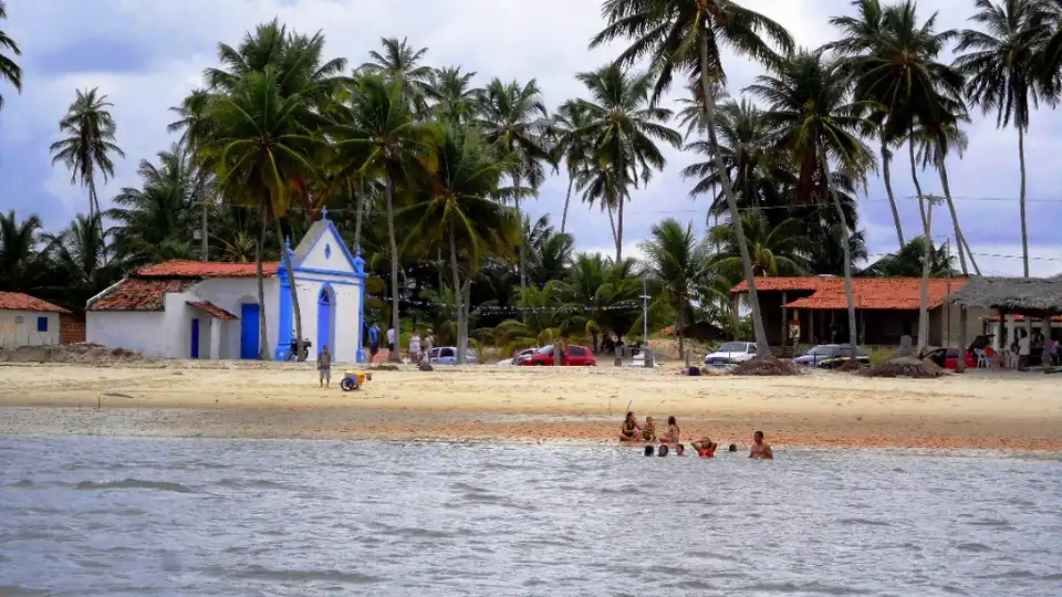 Praia de Coqueirinho no Conde, PB — capela branca e azul, coqueirais e banhistas na água calma